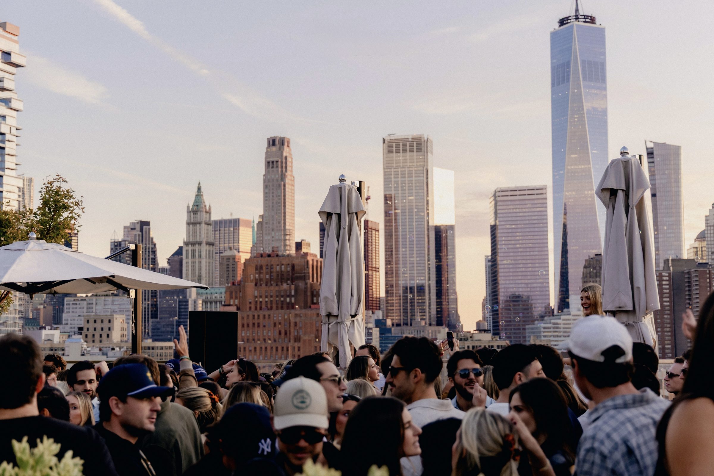 Packed rooftop crowd at treehouse. NYC — One WTC skyline golden hour